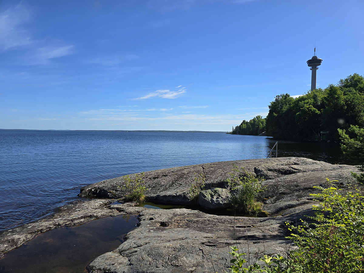 Kallioinen ranta ja väreilevää sinistä Näsijärven vettä. Oikealla näkyy Näsinneula.