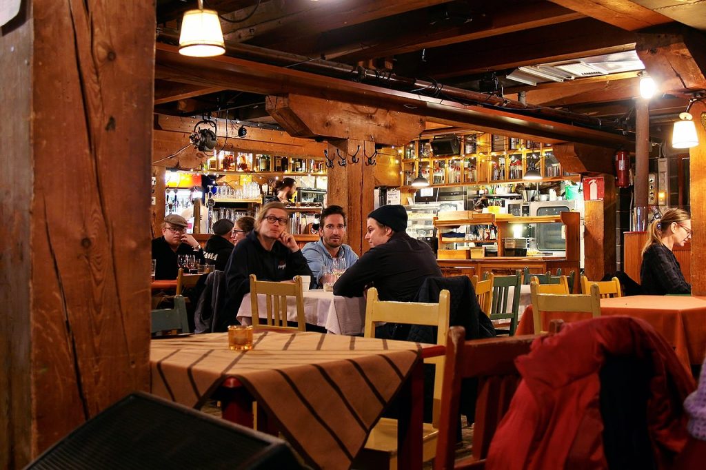 Teatteri Telakan asiakkaita. Hämärä puuseinäinen ja -kattoinen ravintola, jossa paljon keltaisia valoja.